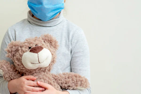 Child is holding Teddy bear wearing protective medical mask on white background. Health care and virus protection concept.
