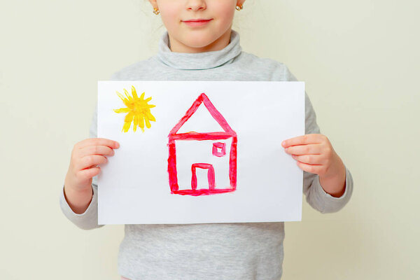 Child is holding picture of red house with sun on yellow background. Elementary school of drawing.