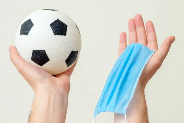 Soccer ball and medical mask in man hands up on white background.