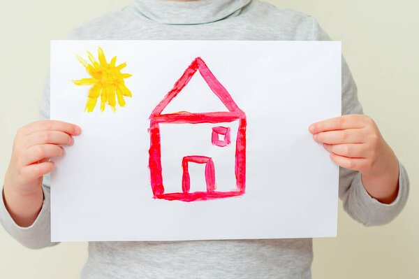 Closeup of child is holding picture of red house with sun at elementary school. Painting concept.