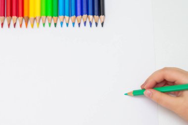 Boş kağıda renkli kalemler çizmek ve çizmek için elinde yeşil renkli kalem tutan çocuğun üst görüntüsü. Metin için alanı kopyala.