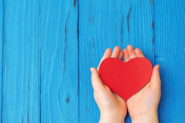 Mavi ahşap masa arkasında kırmızı kalbi destekleyen genç çocukların en iyi görüntüsü. Anneler Günü kutlaması için boş alan.