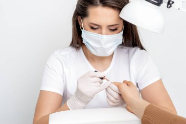 Manikürcü koruyucu maske takıyor. Manikür salonunda kadın tırnaklarını ojeyle boyuyor..