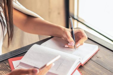 İş kadını, kafenin penceresinin yanındaki akıllı telefonu kullanarak kalemle günlük tutuyor..