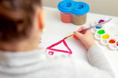 Beyaz kağıda evin çatısını çizen bir çocuğun eli. Yaratıcı öğrenme kavramı.