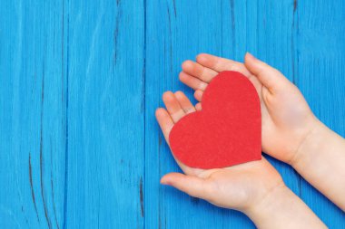 Mavi ahşap masa arkasında kırmızı kalbi destekleyen genç çocukların en iyi görüntüsü. Anneler Günü kutlaması için boş alan.