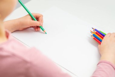 Sevimli küçük çocuk elinde renkli kalemlerle beyaz kağıda yeşil kalemle resim çiziyor. Seçici odak.
