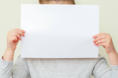 Beyaz arka planda, çocuğun elindeki boş bir kağıdın yüzünü kapatıyoruz. Çocuğun elindeki kağıt maketi..