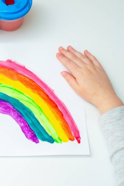 Koronavirüs salgını karantinası sırasında kağıt üzerinde gökkuşağı olan bir çocuğun eli..