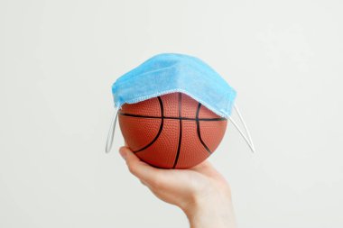 Arka planda tıbbi maskesi olan basketbol topunu tutan adamın eli. Basketbol yarışmalarının iptali.