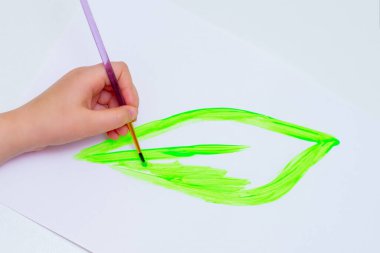 Çocuk beyaz kağıda suluboya ile yeşil yaprak çizer. Dünya günü ve çevre koruma kavramı.