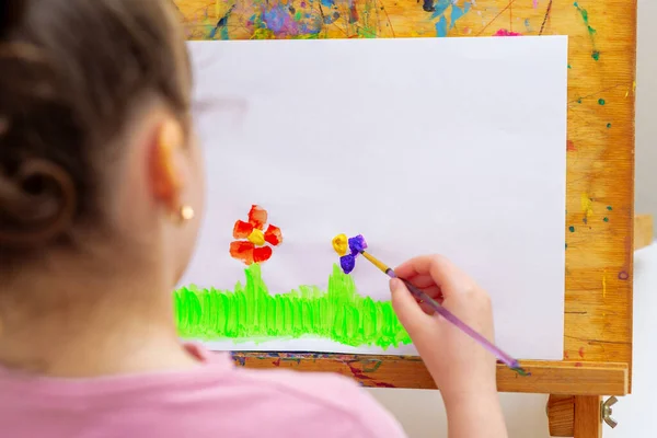 緑の草の上に花を描く少女の手と白紙の上に水彩で筆でイーゼル — ストック写真