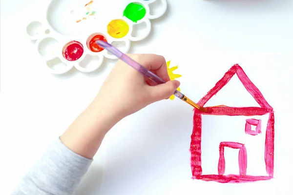 筆で子供の手の上からの眺めは 白い紙に水彩でカントリーハウスの絵を描いています サイドビュー — ストック写真