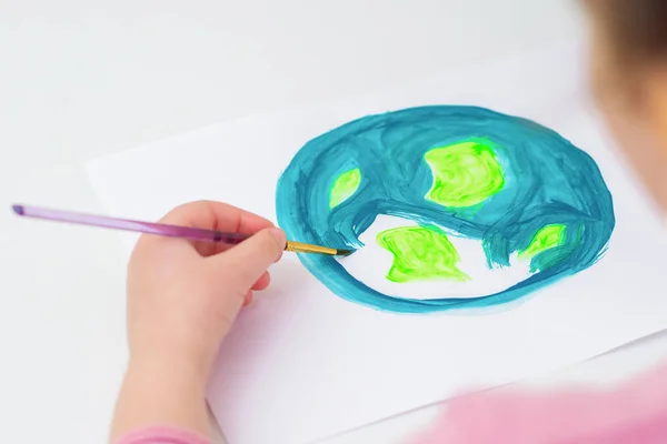 地球の絵を描く子供の手を閉じてください 子供は白い紙にアクリル色で筆で地球を描いています 地球の日のコンセプト — ストック写真