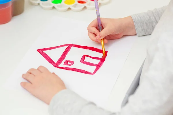 鉛筆で子供の手の側面図は 白い紙に赤い家の絵を描いています — ストック写真
