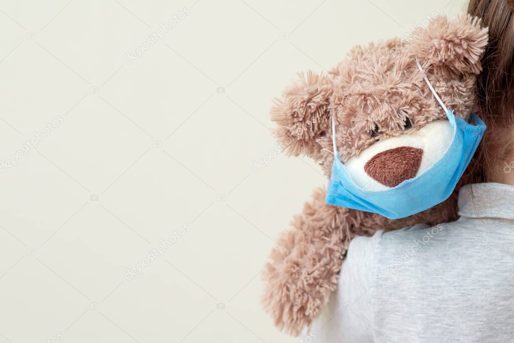 Soft toy bear with protective medical mask on child shoulder. Health care and virus protection concept.