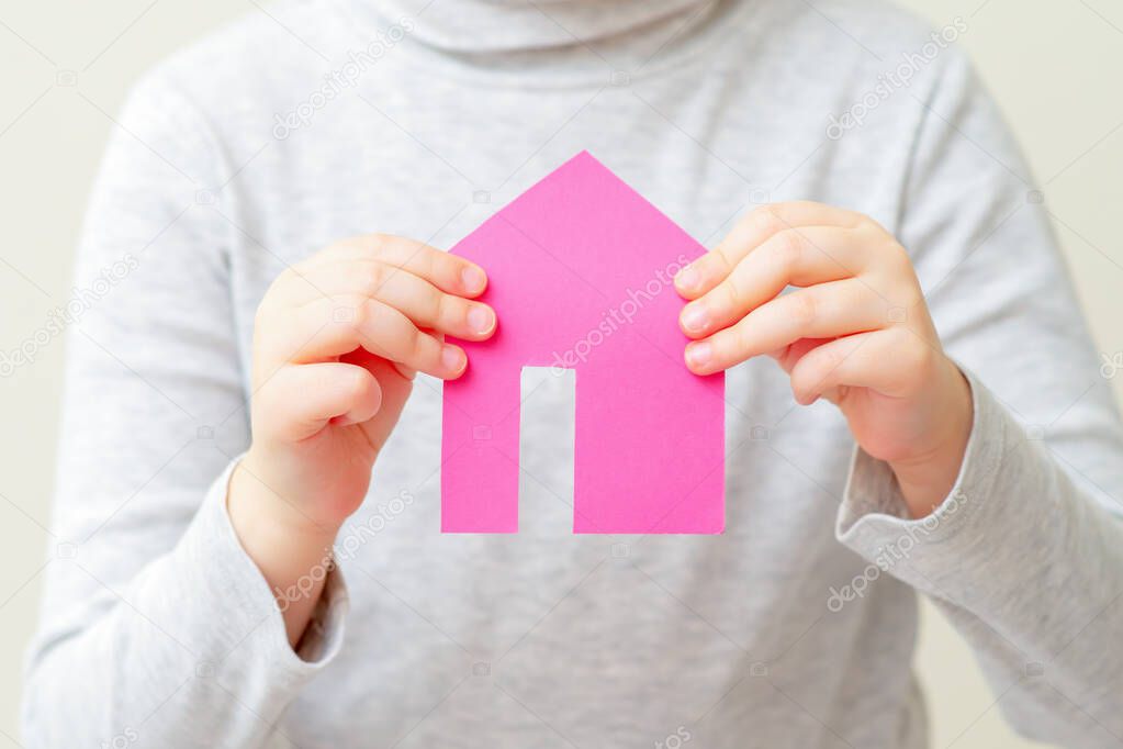 Child's hands holding paper pink house dreaming of his own home. Housing and family concept.