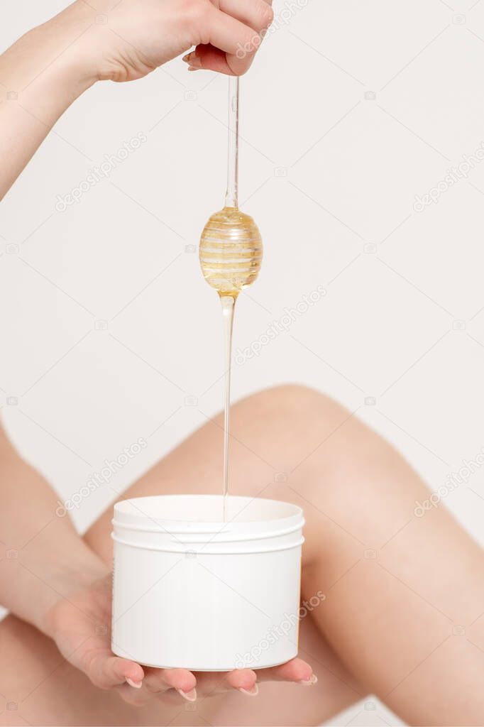 Woman holding honey stick while flowing down liquid wax into container on white background.