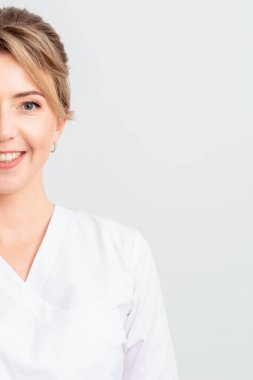 Beyaz cüppeli güzel bir doktor, stajyer ya da kozmetik uzmanının yarım portresi beyaz arka planda izole bir şekilde kameraya gülümsüyor..