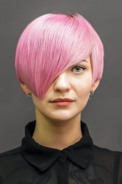 Koyu gri arka planda pembe kısa saçlı güzel bir genç kadının portresi..
