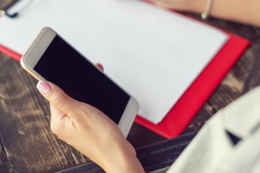 Kafede beyaz bir kağıdın arka planında beyaz siyah ekranlı beyaz cep telefonu tutan bir kadının görüntüsü..