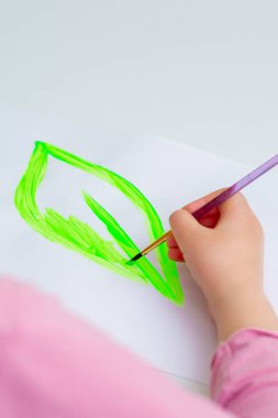 Çocuğun eli, beyaz kağıda suluboya fırçayla yeşil yaprak çiziyor. Dünya Günü konsepti.