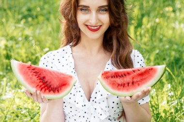 Elinde iki dilim karpuz olan genç bir kadının portresi yeşil çimlerin üzerinde gülümsüyor..