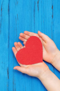 Mavi arka planda kırmızı kalbi tutan çocuk elleri, bağış konsepti.