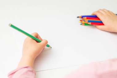 Elinde bir demet renkli kalem tutan yeşil pancil kağıtların üzerine beyaz kağıt çizen bir çocuk eli. Seçici odak.
