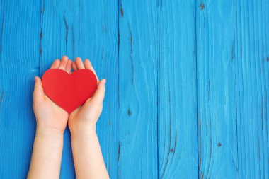 Ahşap arka planda kırmızı kalpli çocuk elleri. Kardiyoloji konsepti. Uzayı metin için kopyala. Üst görünüm.