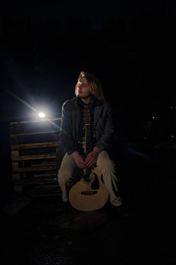 Akşamın geç saatlerinde elinde gitar olan genç bir adam.