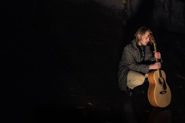 Akşamın geç saatlerinde elinde gitar olan genç bir adam.