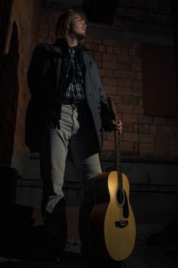 Akşamın geç saatlerinde elinde gitar olan genç bir adam.