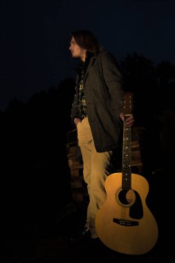 Akşamın geç saatlerinde elinde gitar olan genç bir adam.