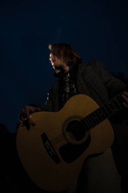Akşamın geç saatlerinde elinde gitar olan genç bir adam.