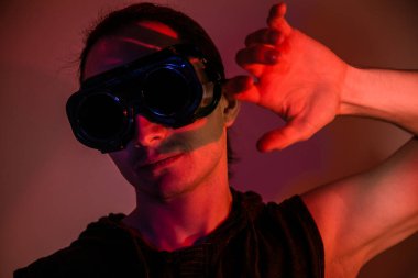 Kaynak gözlüklü bir adam kırmızı arka planda dumanlı.