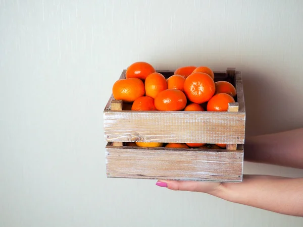 Niña sosteniendo una caja de mandarinas, sobre un fondo neutro, espacio para el texto — Foto de Stock