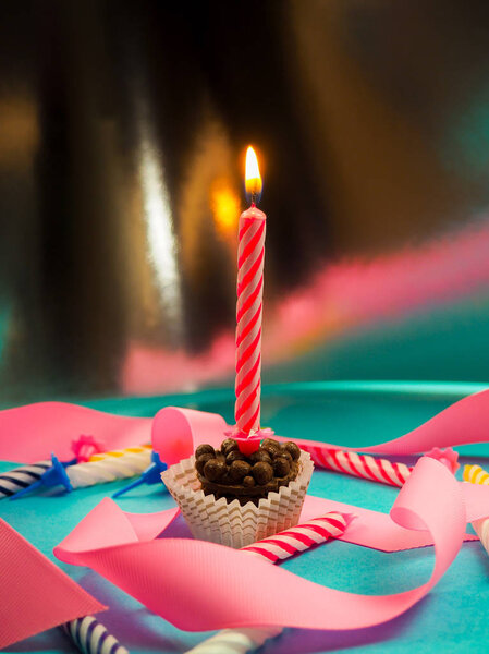 свеча на день рождения горит на заднем плане другие свечи, розовые ленты, праздничная атмосфера
