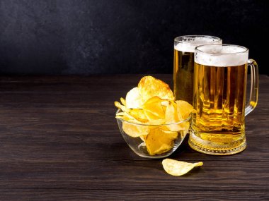 iki cam bardak light bira ve cips koyu ahşap bir masa üzerinde bir cam kasede