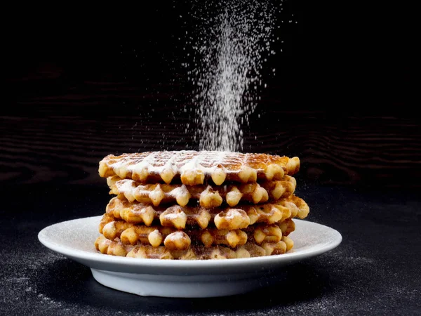 Beyaz plaka ile üstüne pudra şekeri siyah arka plan, çok lezzetli aperatif üzerine döktü eleme ev yapımı Belçika waffle. eski ahşap masa üzerinde şeker. Karanlık rustik tarzı. kopya alanı, şık