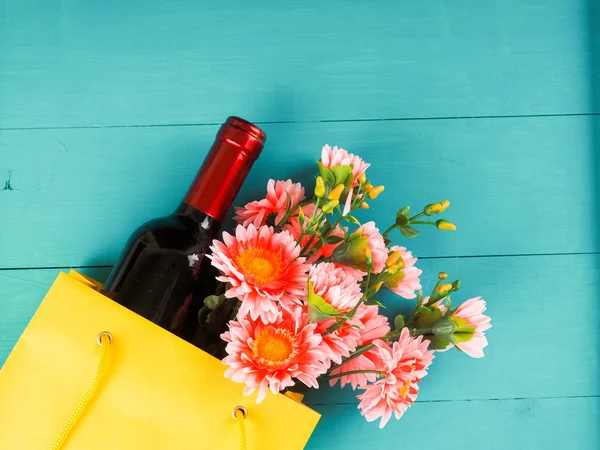 bottle of wine and flowers in the package on wooden background, space for text