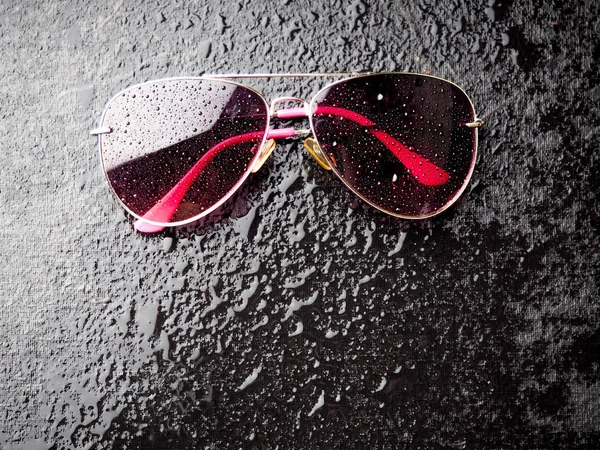 Stylish pink sunglasses with drops of water, the concept of leisure on black a stylish background — Stock Photo, Image