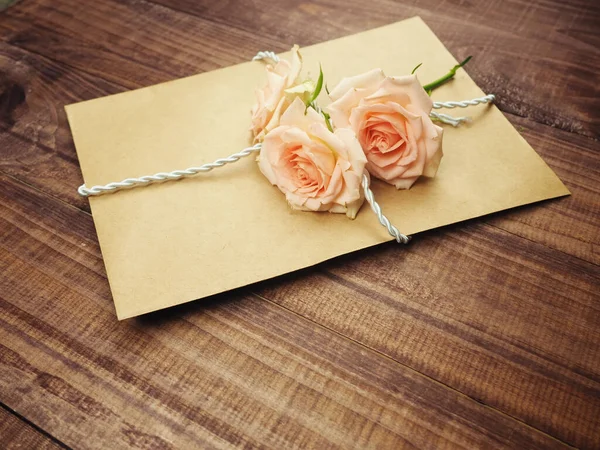 Kraftpapier envelop, oud papier gebonden met touw, oud touw, bovenop zachtroze rozen, het concept van een geschenk, een verrassing. Gefeliciteerd met Valentijnsdag, gefeliciteerd. Ik hou van je. — Stockfoto