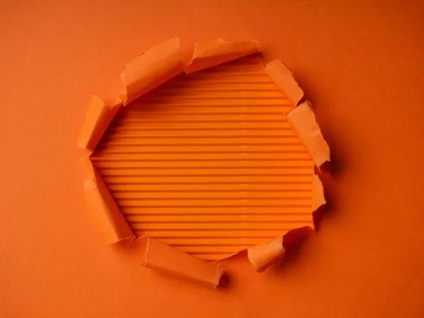 Small paper hole with torn sides over orange background for your text, print or promotional content. Through paper. Ripped hole. No people. Accurate shot. Advertising and breakthrough concept