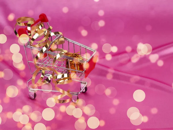 Árbol de Navidad en el carrito de compras en el fondo de satén rosa brillante como fondo, fondo de seda, tarjeta de Navidad. Feliz año nuevo saludos, regalos, símbolos de Navidad en seda rosa — Foto de Stock