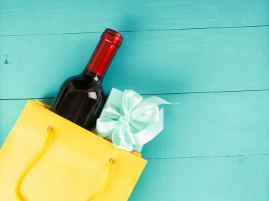 Hediye olarak sarı bir paket şarap, sonraki çiçekler, hediyeler, fotokopi alanı, mavi ahşap arka plan, kızlara çıkma teklifinde bulunmak için.