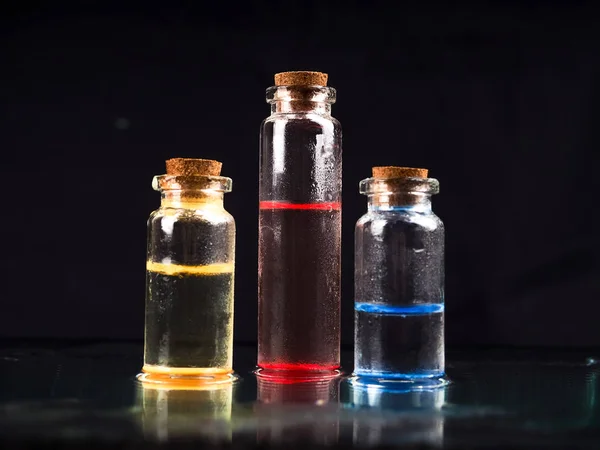 Trzy kolorowe fiolki ze szkła ciekłego z czarnym tłem do badań medycznych. W laboratorium chemicznym Szklana fiolka z korkiem w kolorze czarnym. Kilka małych szklanych fiolek z korkiem — Zdjęcie stockowe