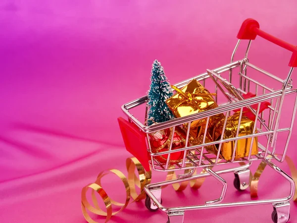 Carrito de compras navideñas con regalo, decoración de vacaciones en rosa pastel vista arriba. Luminoso estilo laico. carrito de compras navideñas con regalo — Foto de Stock