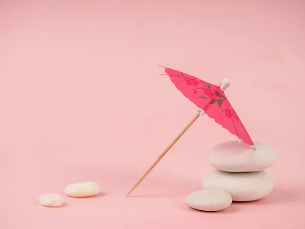 Kokteyl şemsiyesi. Pembe kağıt kokteyl şemsiyesi pembeye izole edilmiş. Pembe taşların üzerinde kağıt pembe şemsiye, beyaz taşların yanında, boş zaman ve minimalizm kavramı..