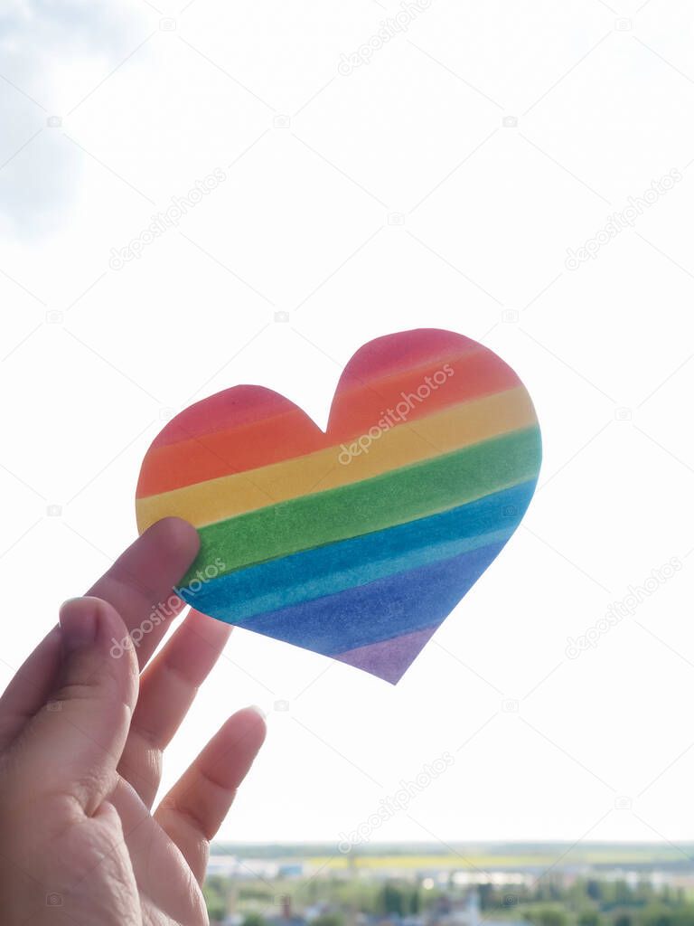 Rainbow Heart, lgbt rights concept, hand holds a heart painted like a LGBT flag, silhouetted against sun.